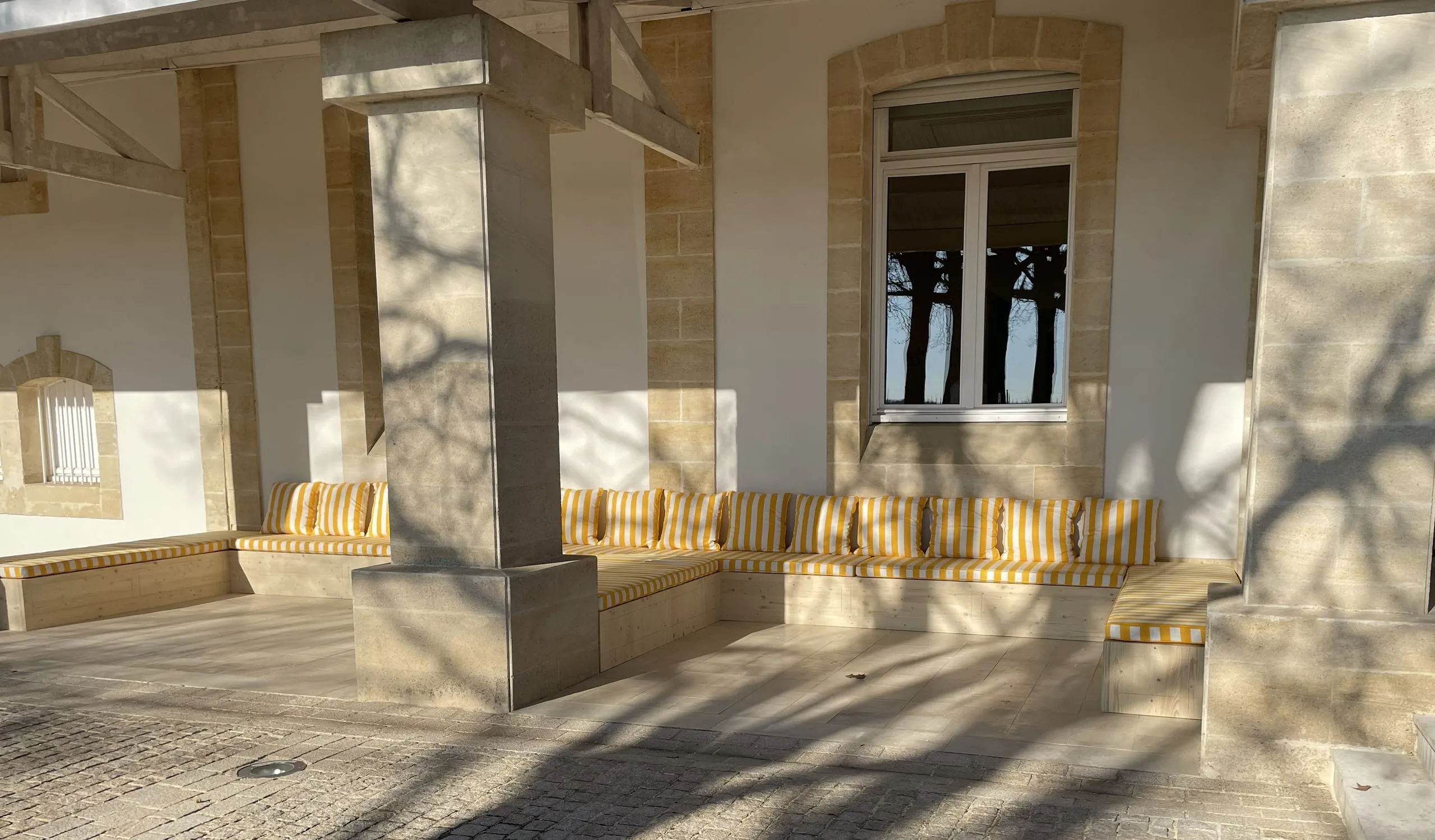 Banquettes en bois avec coussins rayés sous une terrasse couverte en pierre