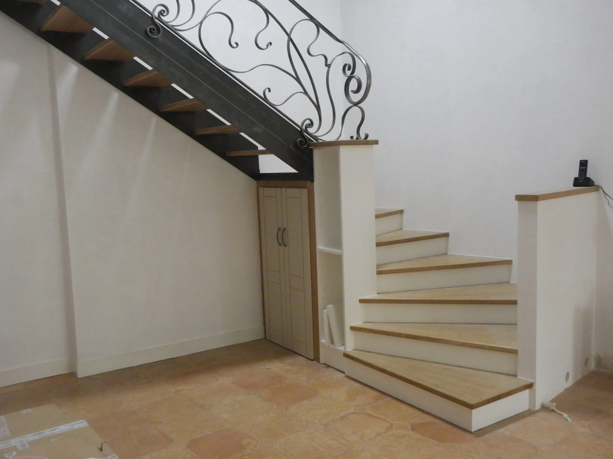 Escalier intérieur aux marches en bois clair et garde-corps en ferronnerie ouvragée
